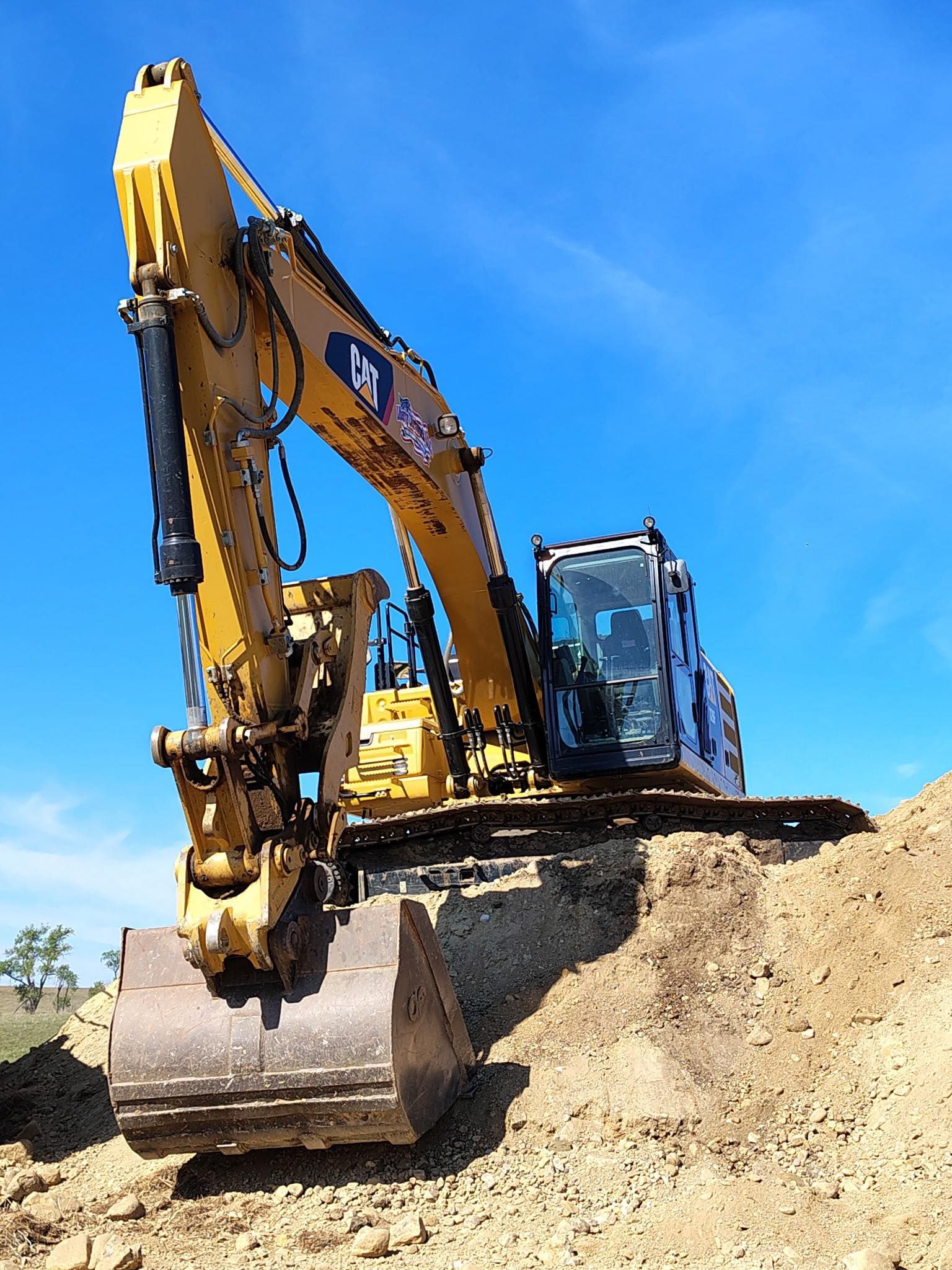 Yellow excavator digging dirt against a blue sky.
