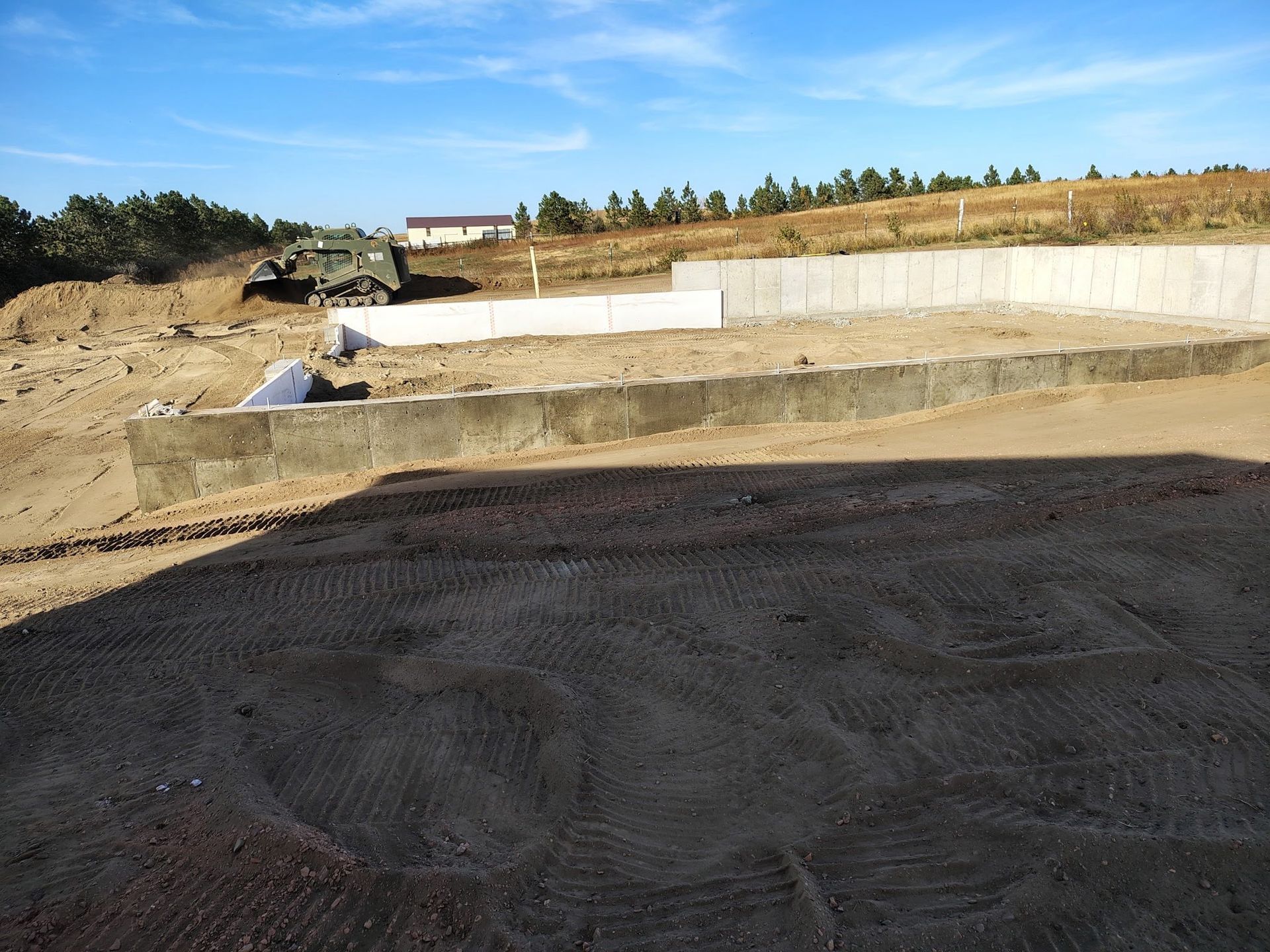Construction site with concrete walls, a vehicle on a hill, and textured ground in sunlight.