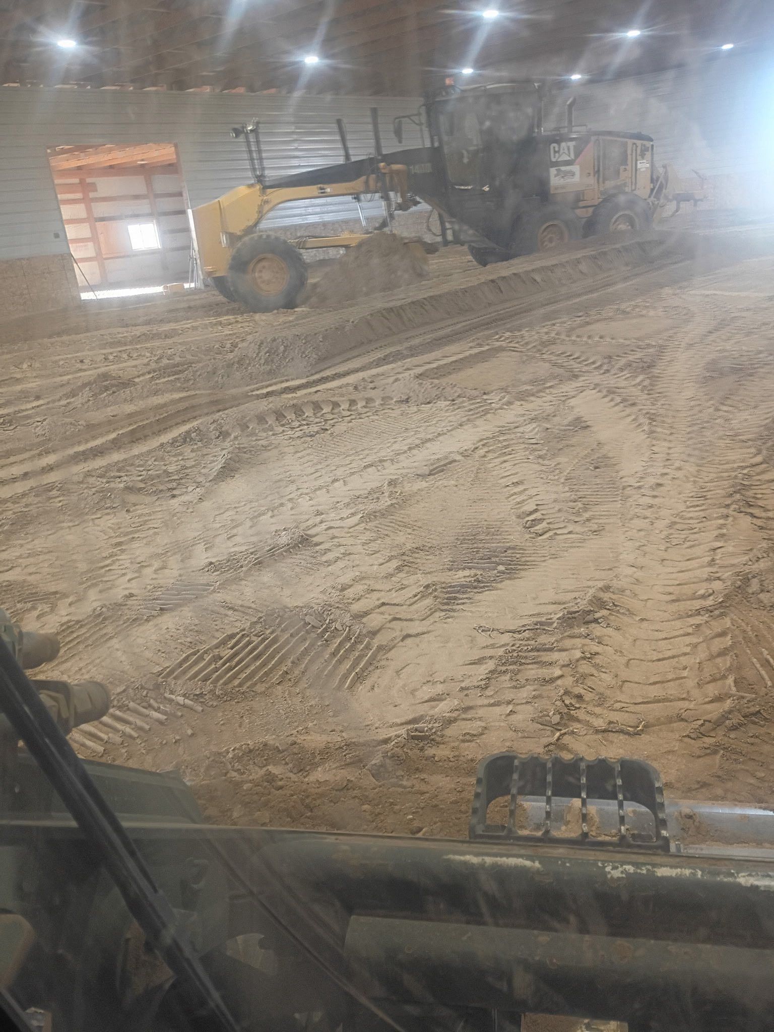 A loader pushing a pile of dirt inside a barn.