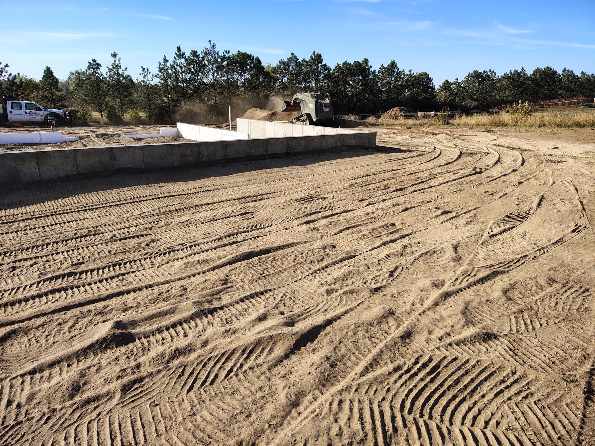 Construction site with concrete foundation, ground covered in tire tracks, a truck in background.