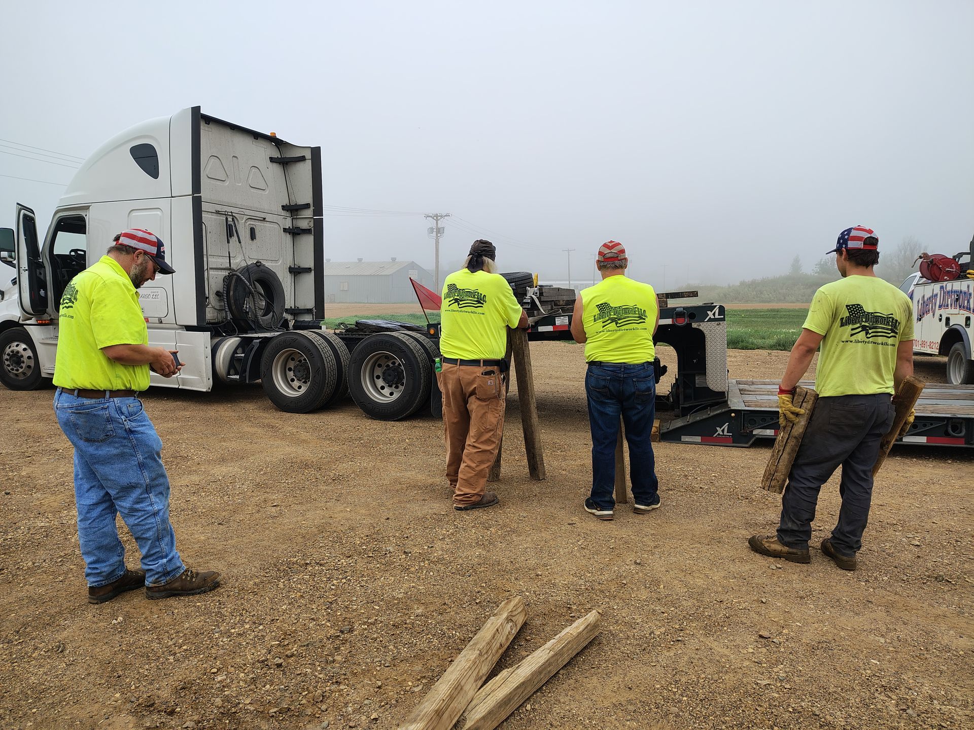 Four people in safety vests working near a truck on a gravel lot.