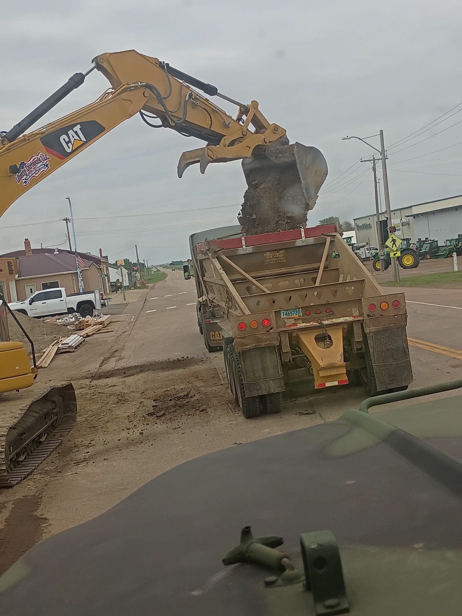 An excavator loads dirt into a dump truck on a street. Cloudy day.