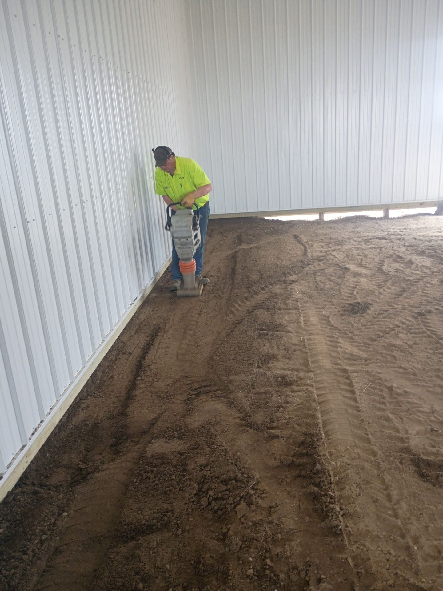 Worker using a plate compactor inside a white building, compacting brown soil.