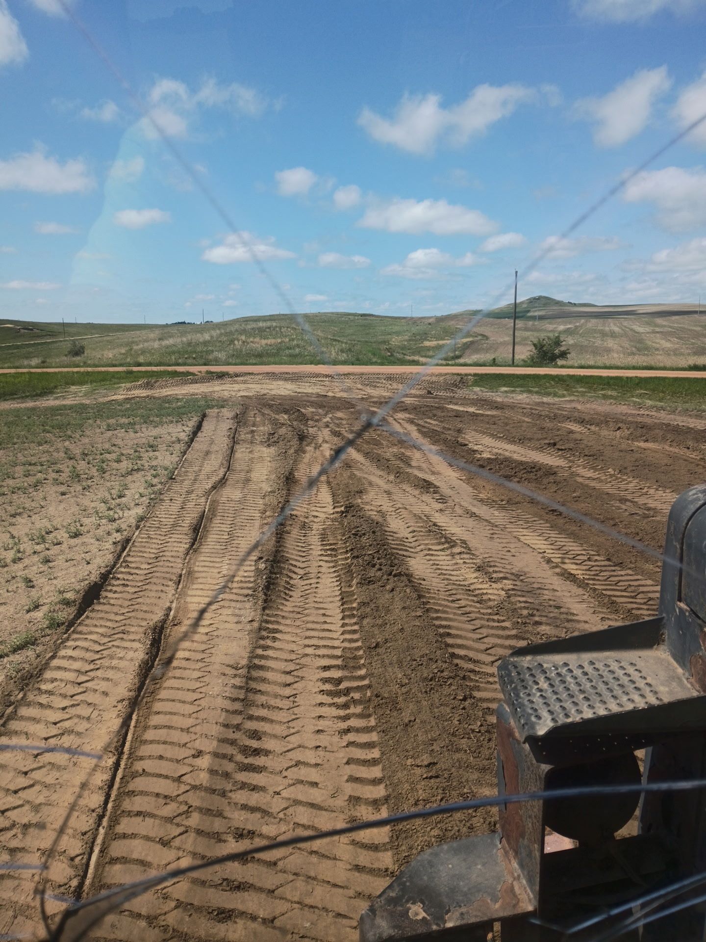 View from a tractor cab of a field with tire tracks under a blue sky.