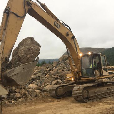 A cat excavator is working on a pile of rocks