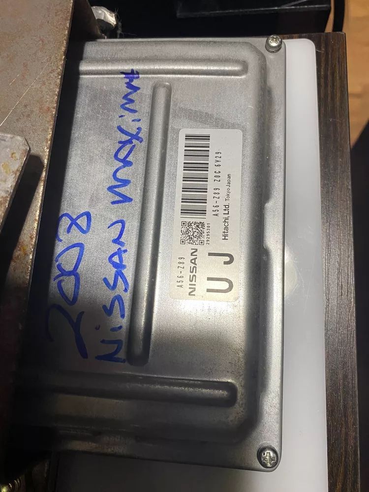 A nissan maxima engine control module is sitting on top of a wooden table.