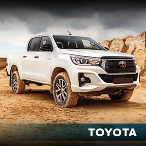 A white toyota hilux truck is parked in the dirt.