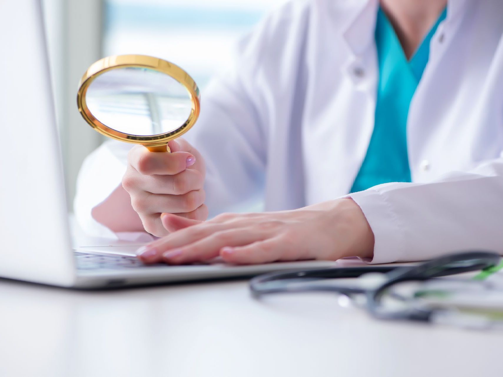 A doctor is holding a magnifying glass in front of a laptop computer.