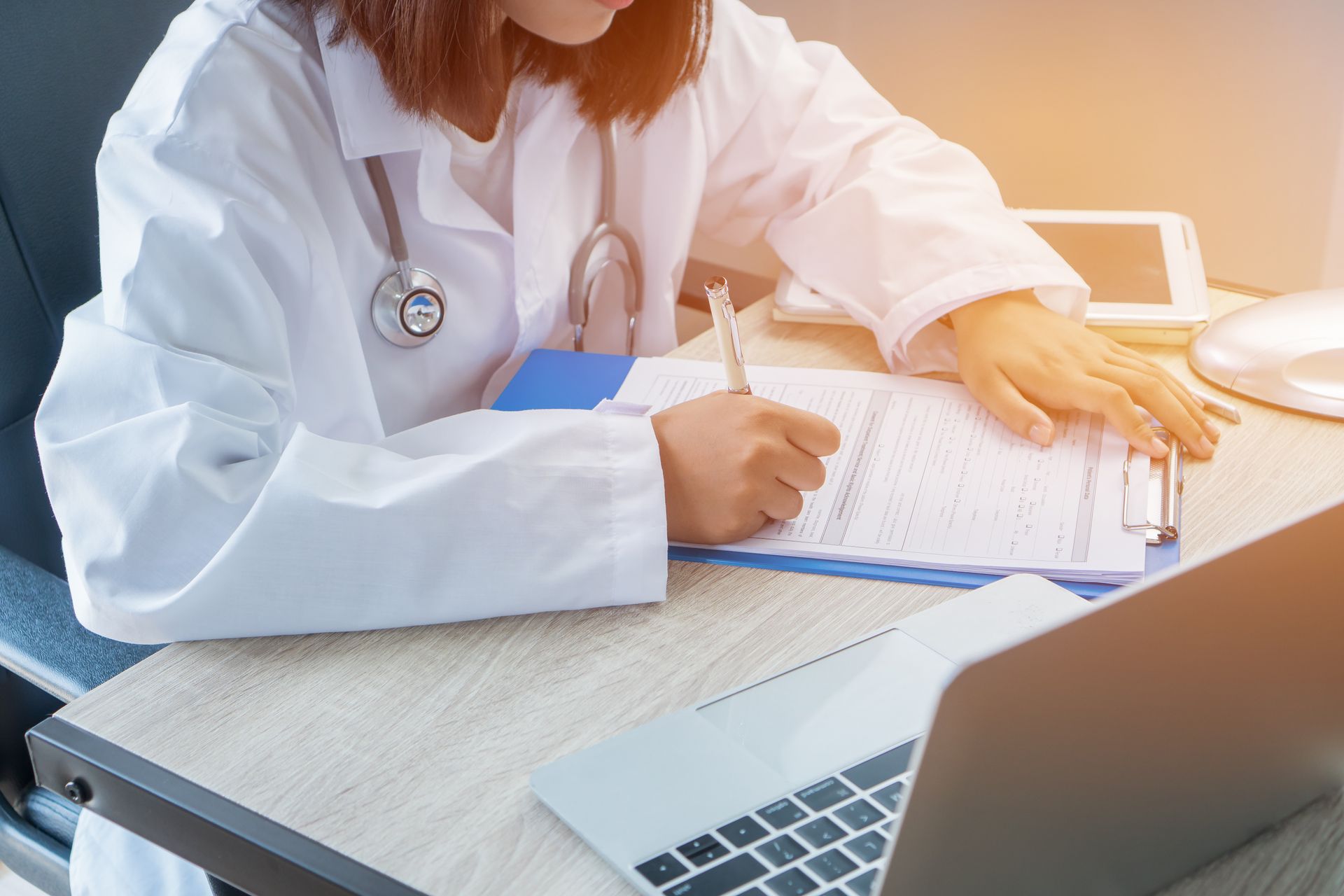 A female doctor is sitting at a desk using a laptop computer.