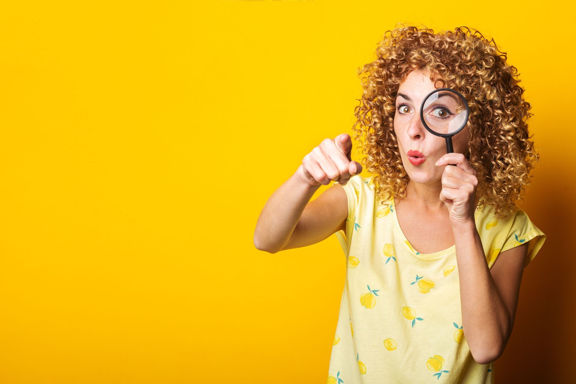 A woman is looking through a magnifying glass on a yellow background.