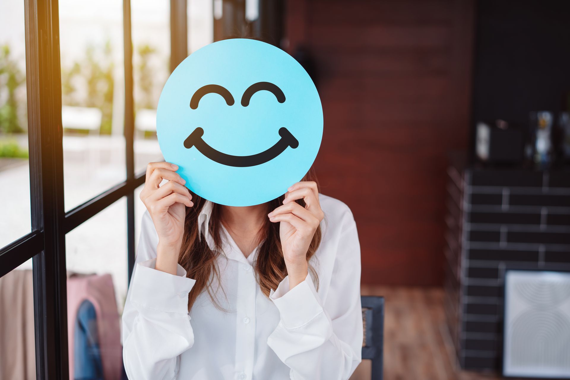 A woman is holding a blue smiley face in front of her face.