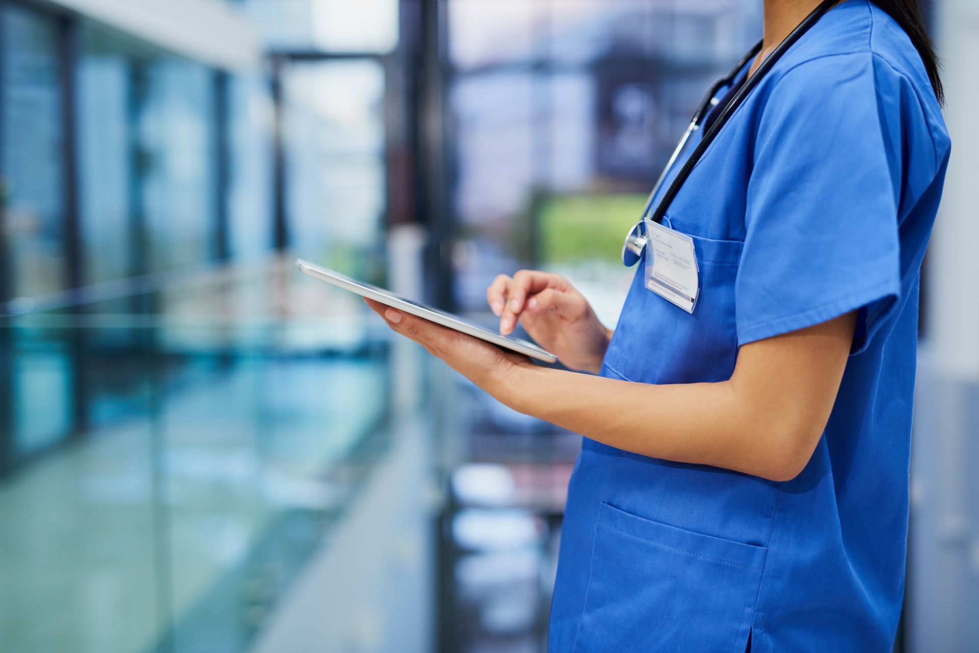 A nurse is using a tablet computer in a hospital hallway.