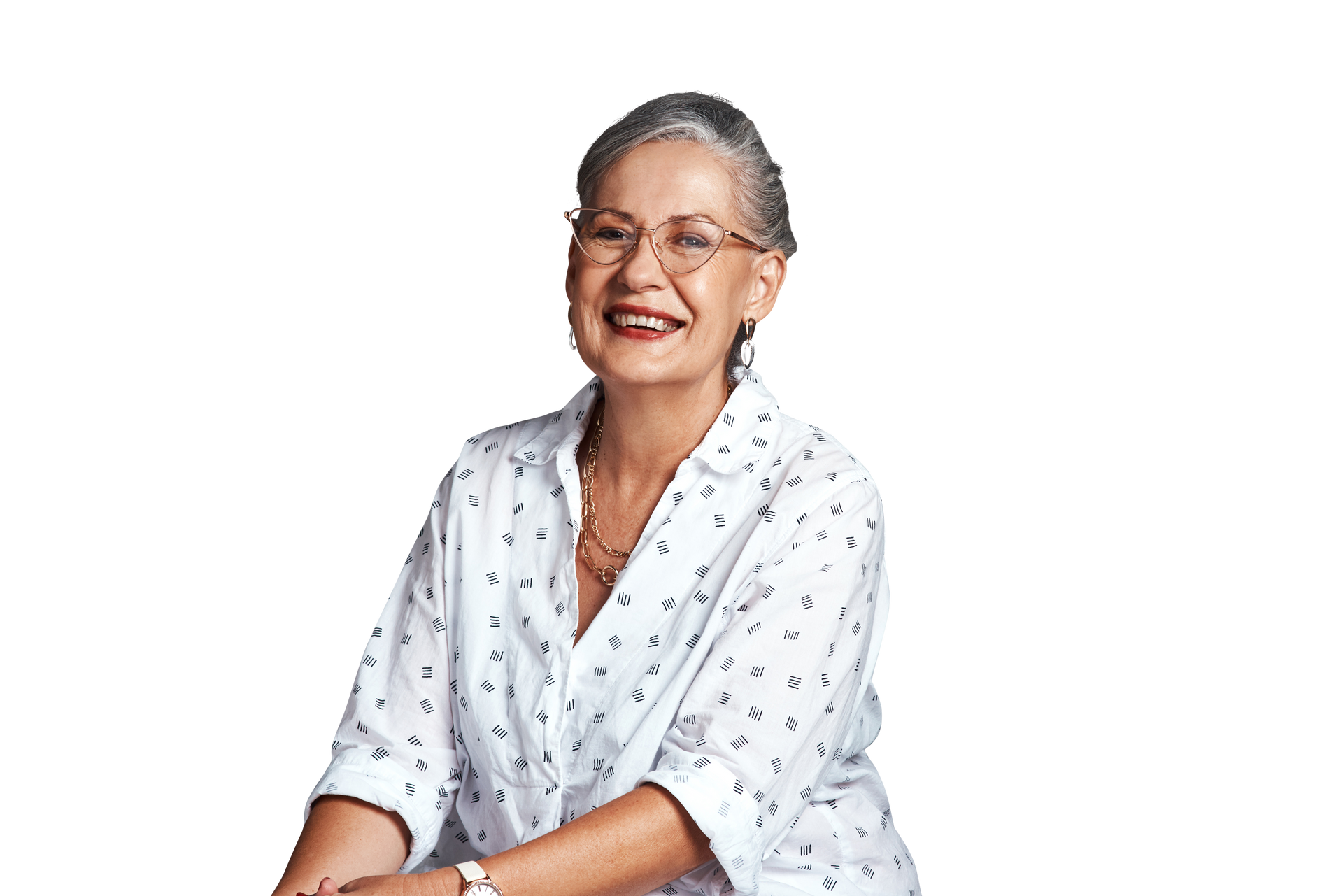 An older woman wearing glasses and a white shirt is sitting down and smiling.