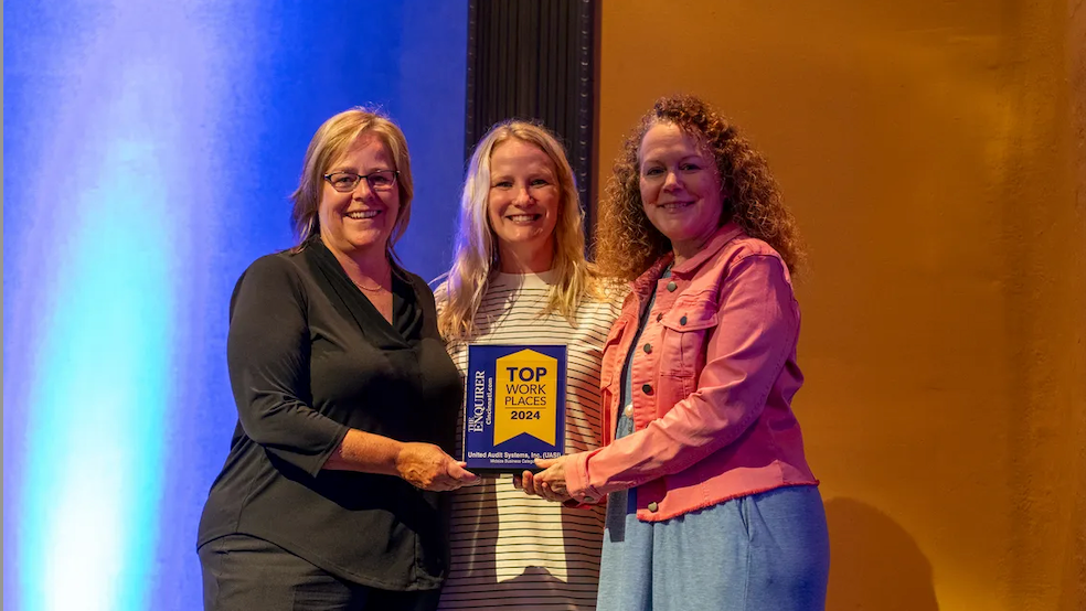 Three women are standing next to each other on a stage holding an award.