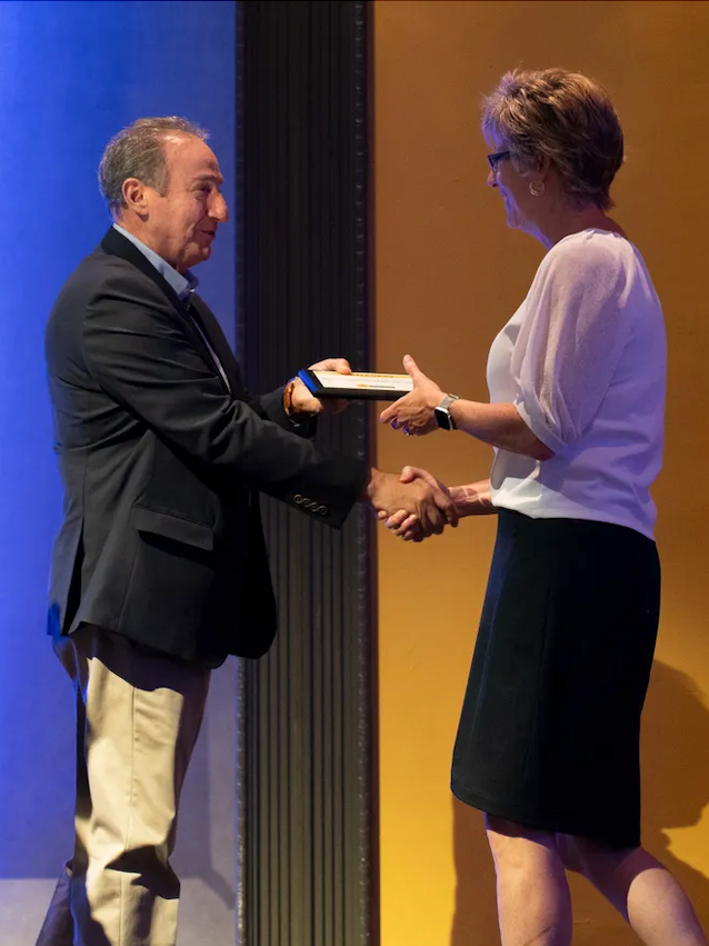 A man is handing a certificate to a woman in front of a sign that says little onsor