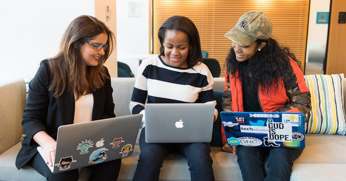 Three women are sitting on a couch using laptops.