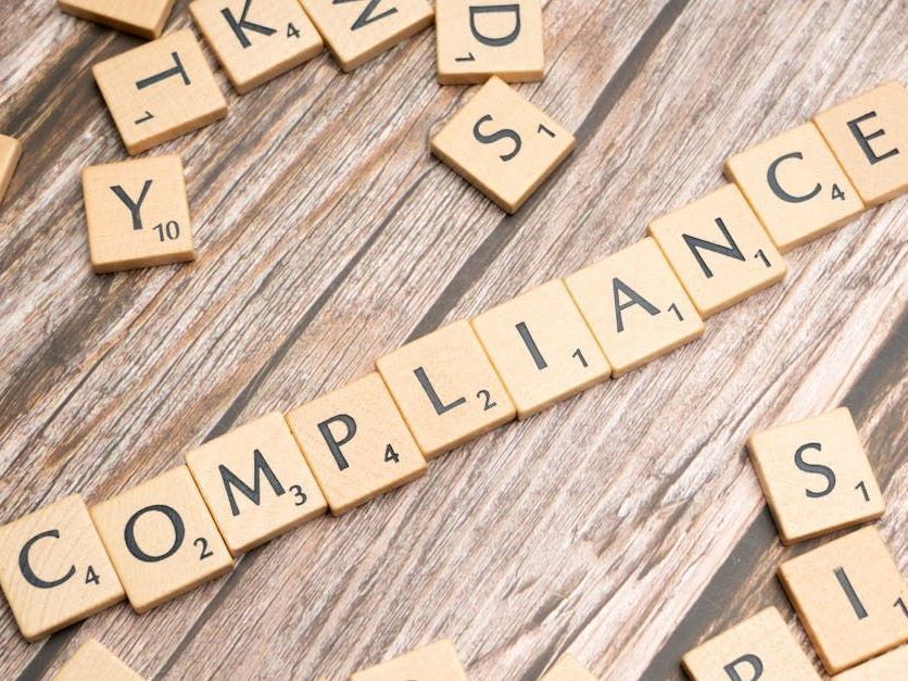 Scrabble tiles spelling out the word compliance on a wooden table