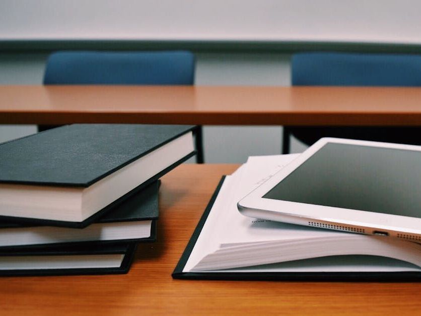 A stack of books and a tablet on a wooden table