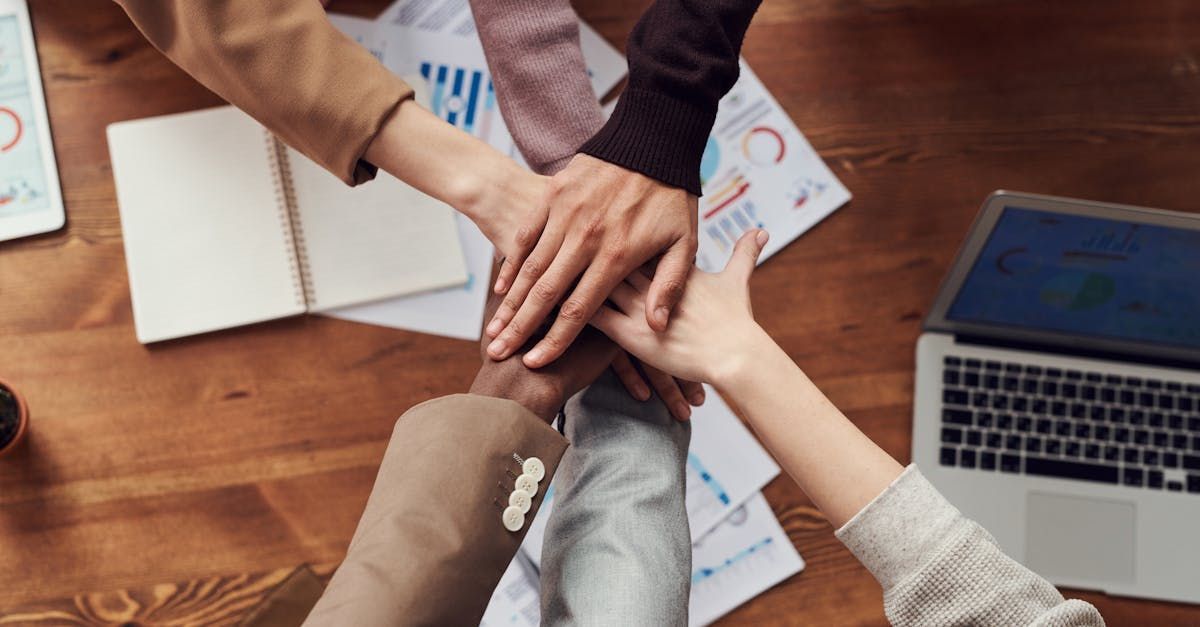 A group of people are putting their hands together on a wooden table.