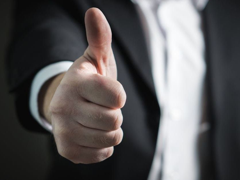 A man in a suit and tie is giving a thumbs up.