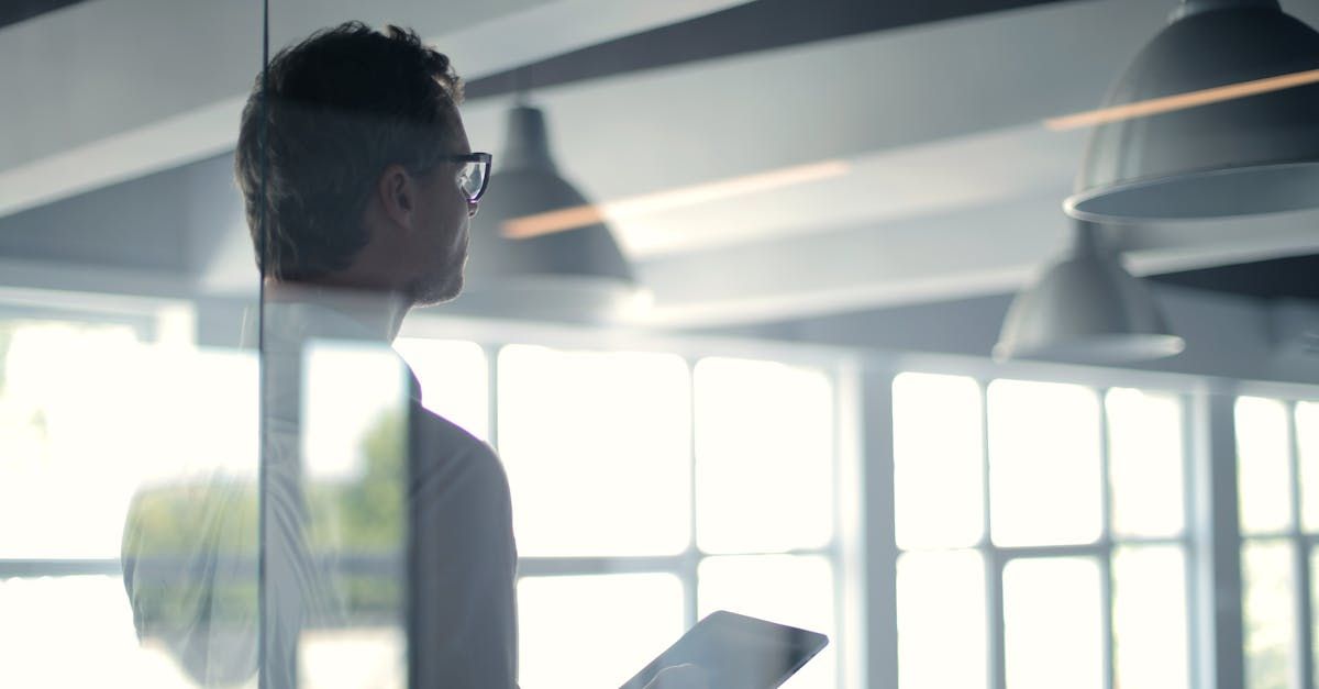 A man is standing in front of a window looking at a tablet.