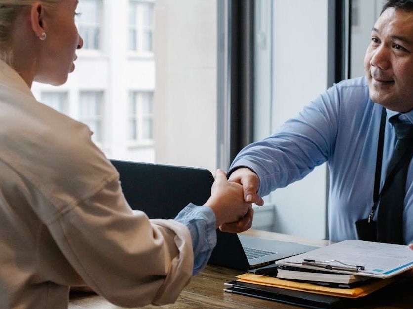 A man and a woman are shaking hands at a table.