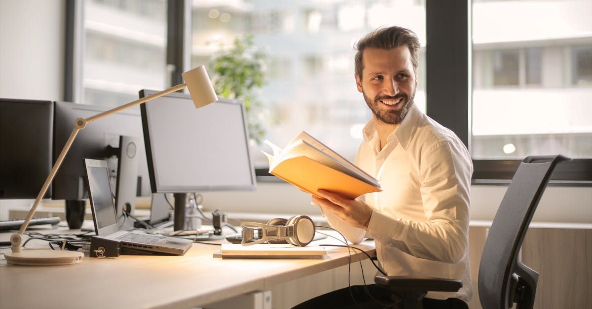 A man is sitting at a desk in an office holding a book.