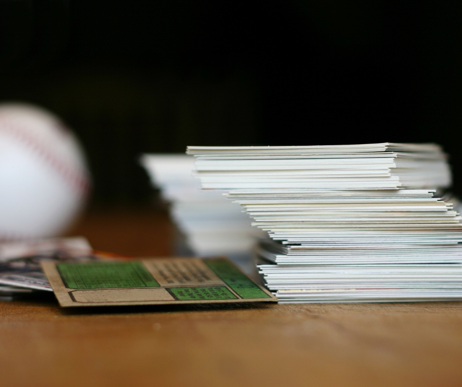 Baseball cards stacked on a wooden surface, baseball in the background.