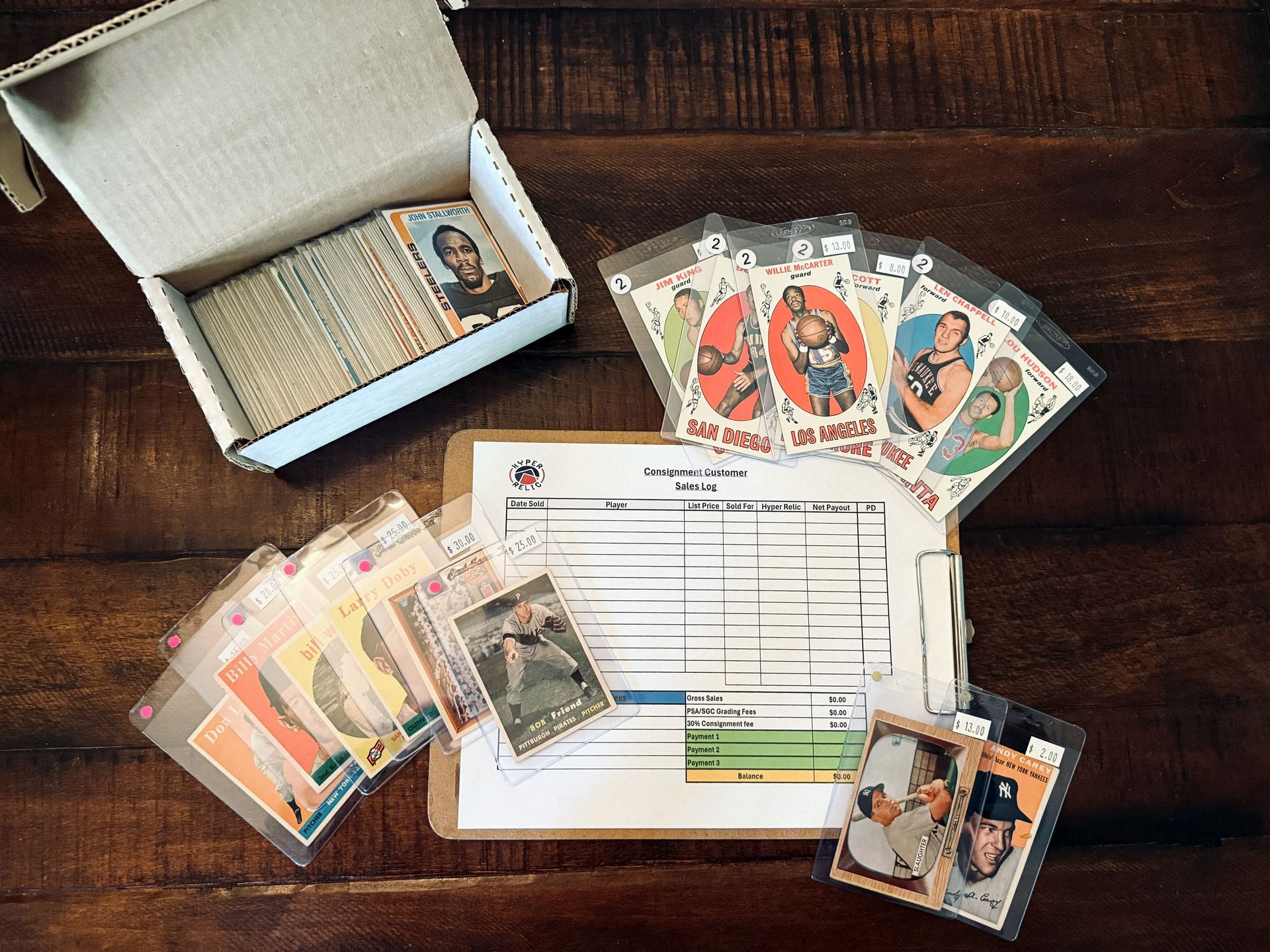 Card collection, baseball cards, in storage box and protective sleeves on wood table with a clipboard.