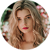 Blonde woman with red lipstick, looking directly at the viewer. Soft, natural lighting with floral background.