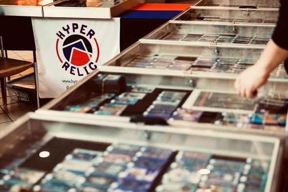 Person browsing cards in glass display cases at a Hyper Relic booth.
