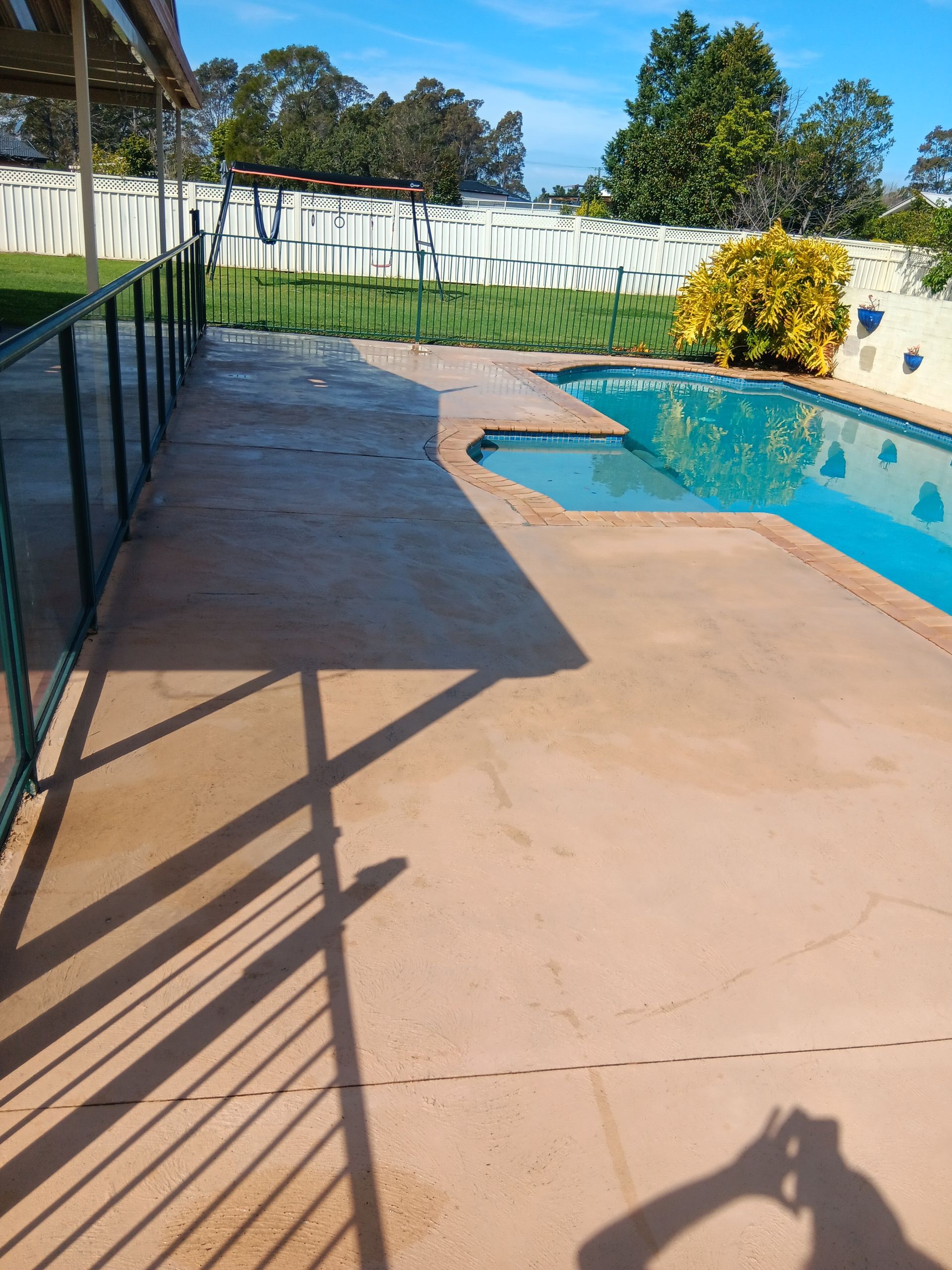 Pool Area With Brown Concrete, Blue Pool, Green Lawn, and White Fence — AMAC Painting & Maintenance Nowra In Nowra, NSW