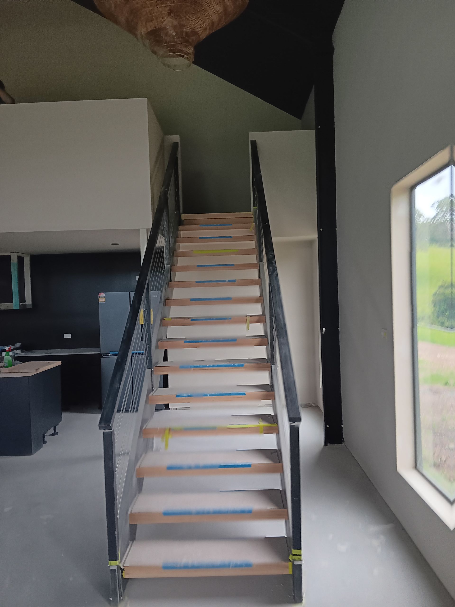 Staircase with wooden steps and black metal railings leads upwards.  Natural light from a window illuminates the space — AMAC Painting & Maintenance Nowra In Nowra, NSW