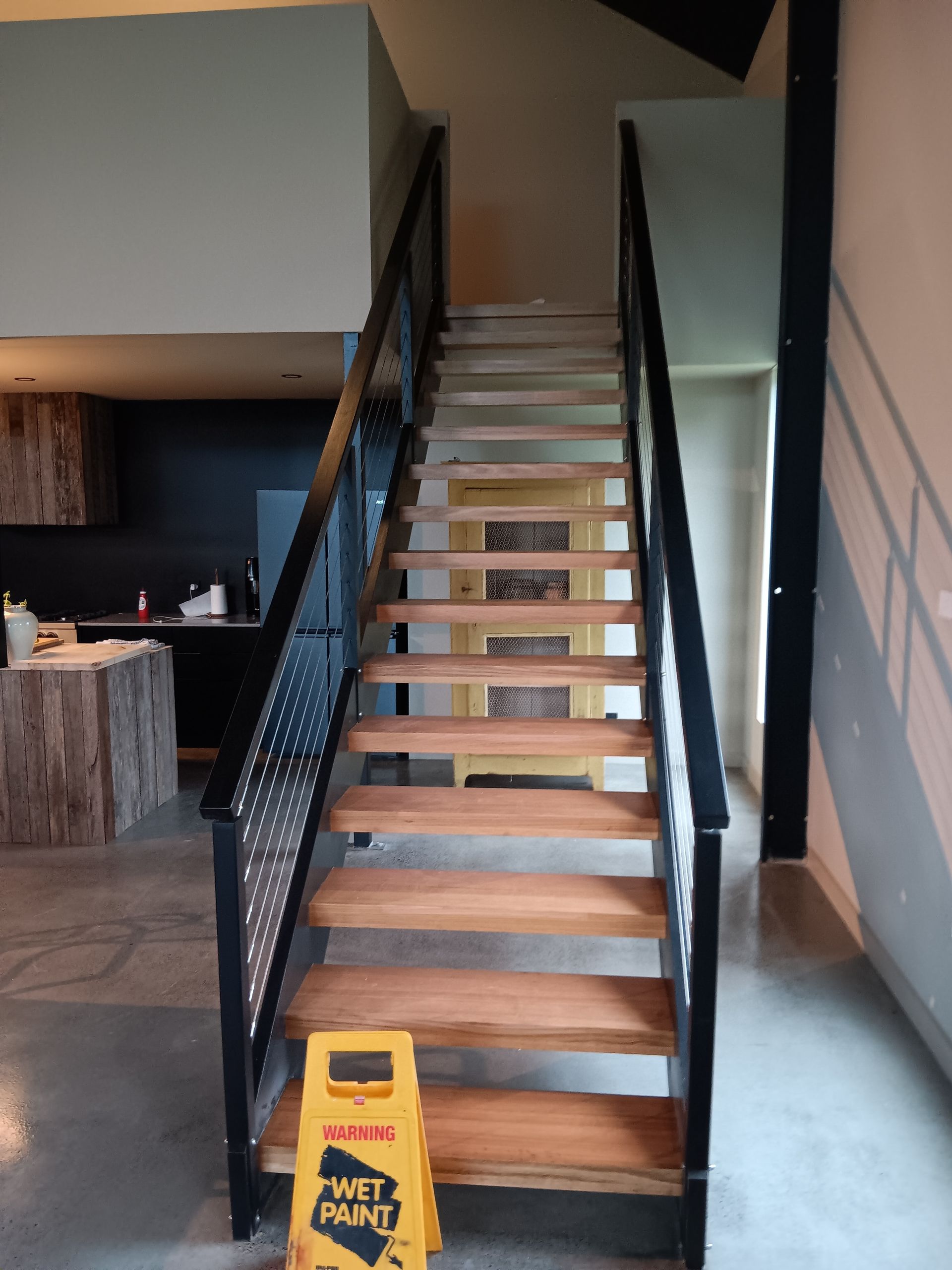 Wooden staircase with black metal railings, a wet floor sign is at the bottom — AMAC Painting & Maintenance Nowra In Nowra, NSW