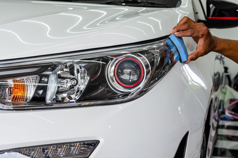 A person is polishing the headlight of a white car.