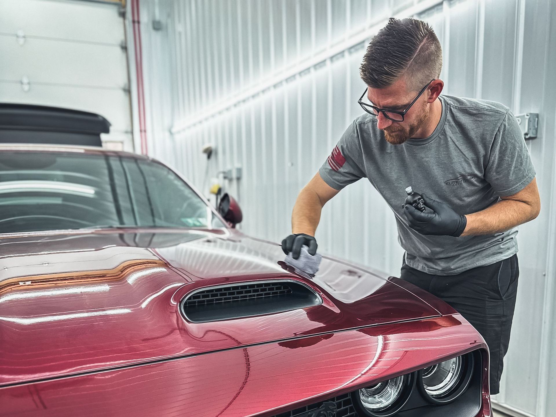 A man is polishing the hood of a red car in a garage.