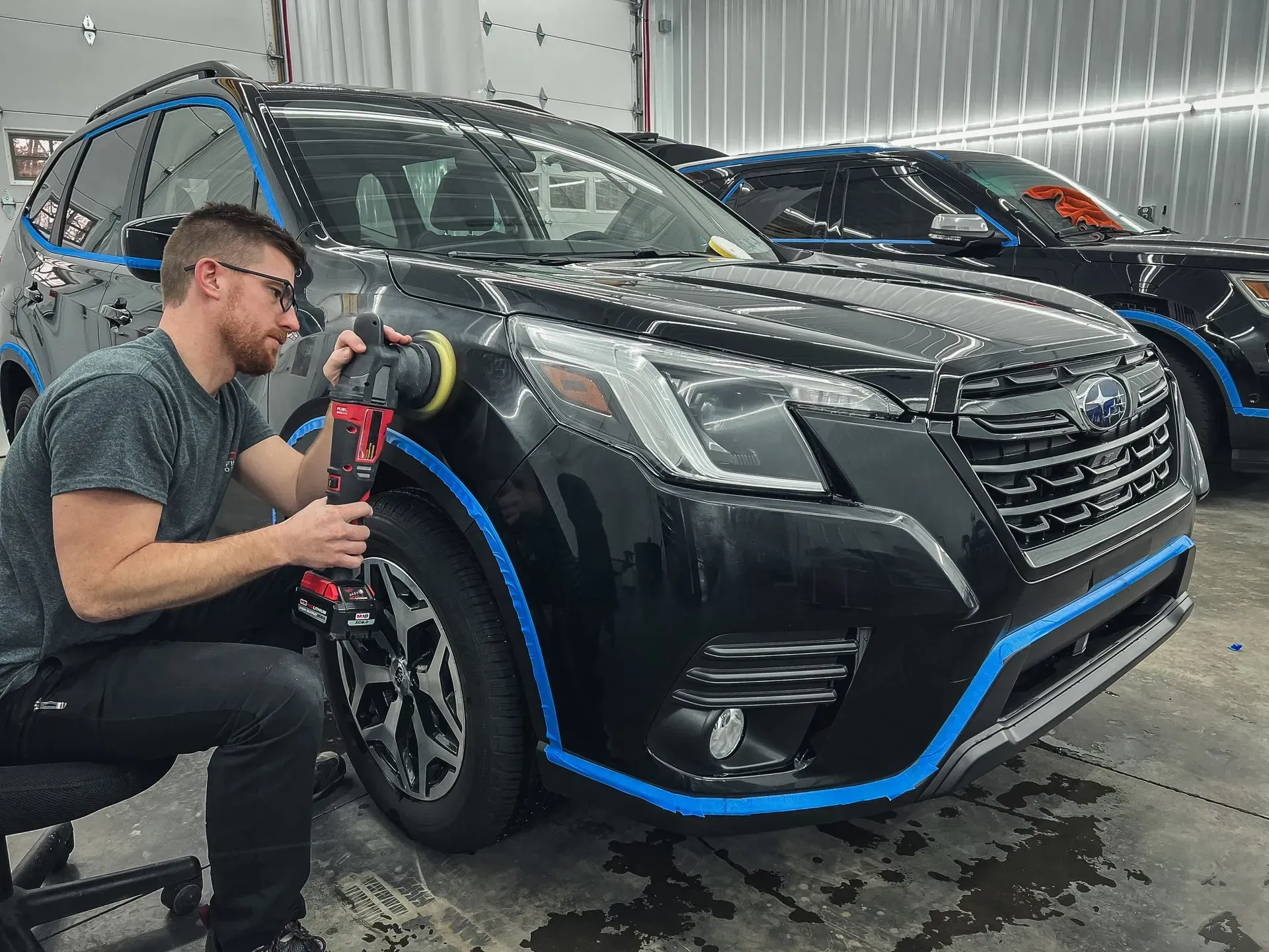 A man is polishing a black suv in a garage.