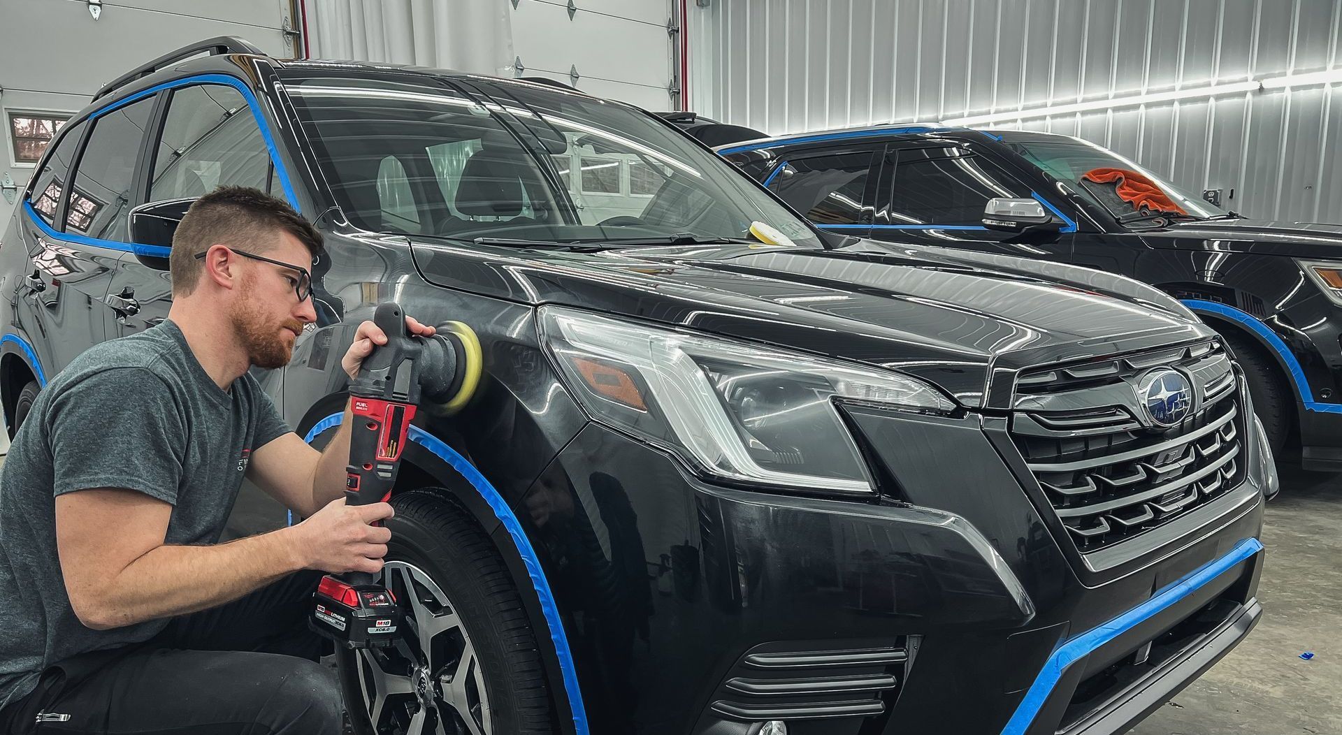 A man is polishing a black suv in a garage.