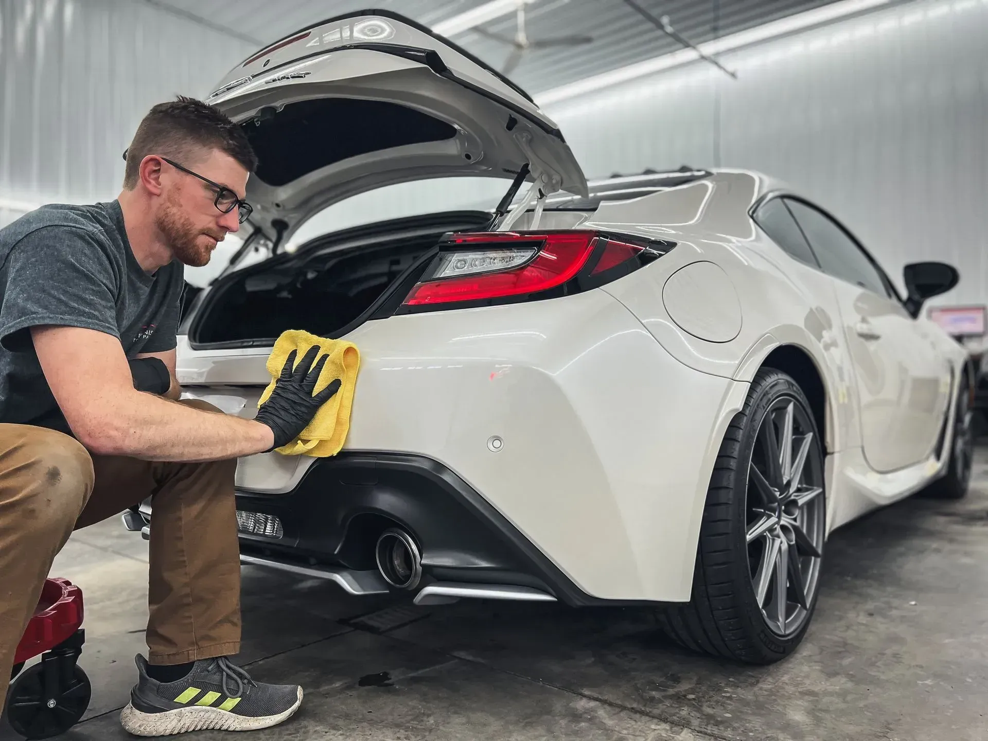 A man is cleaning the back of a white sports car.