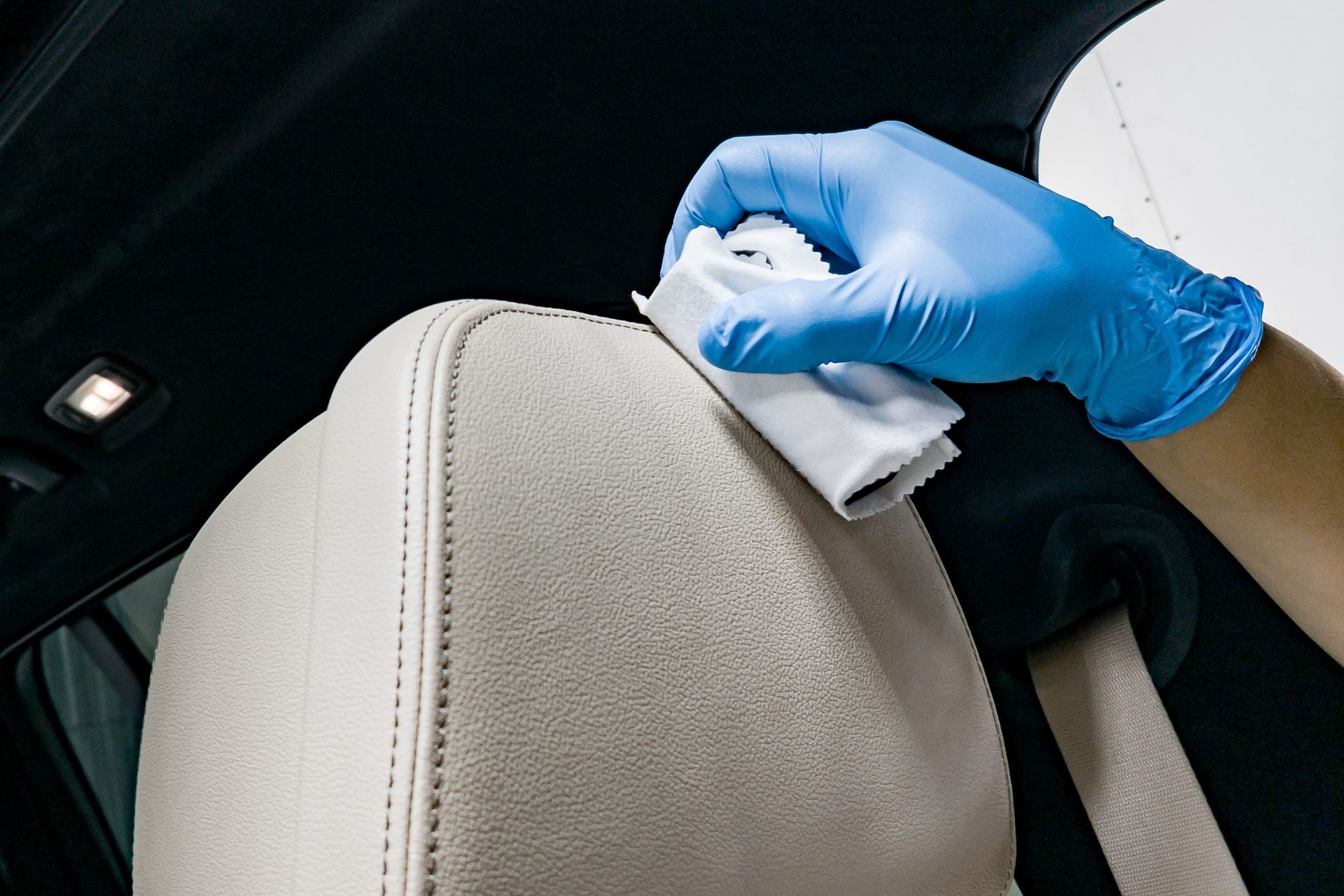 A person wearing blue gloves is cleaning a car seat