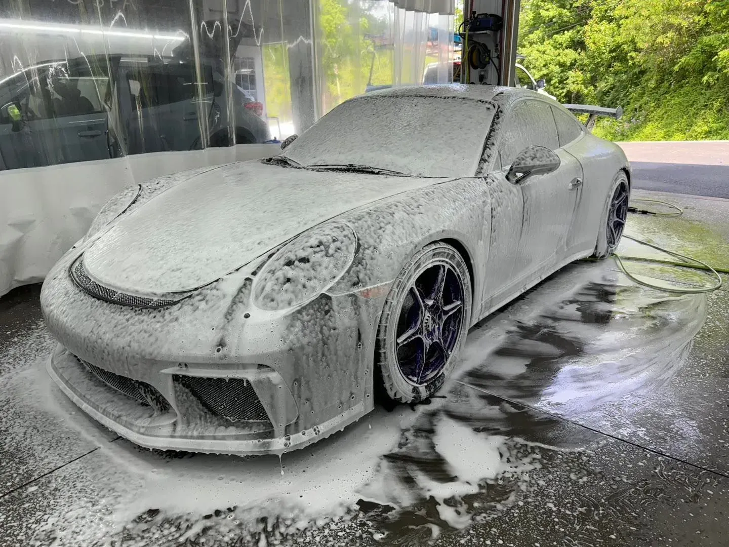 A porsche 911 is covered in foam at a car wash.