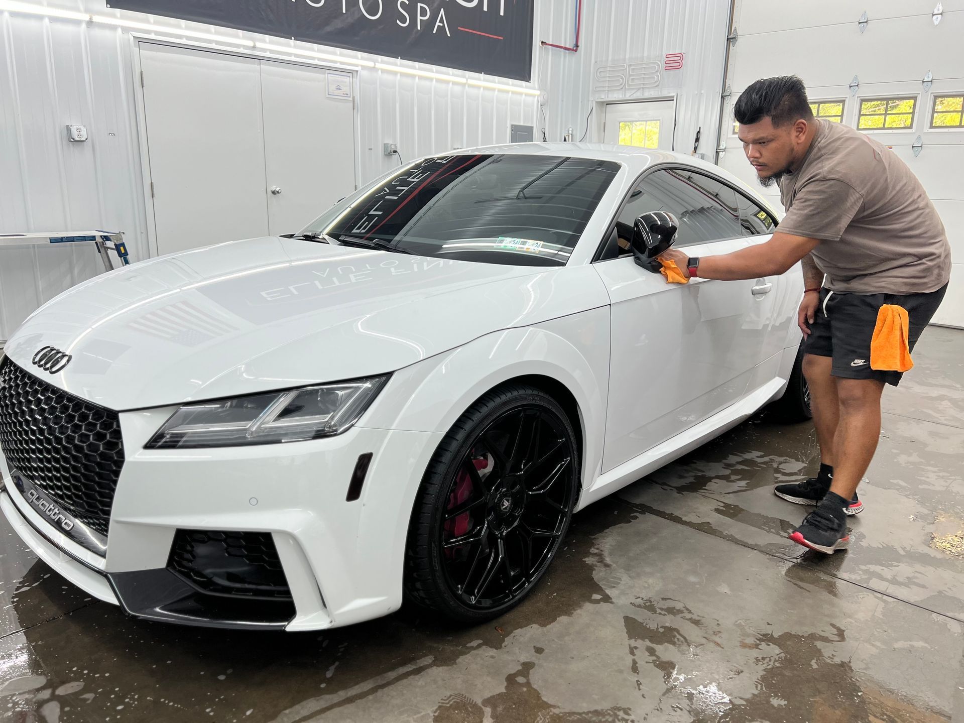 A man is washing a white car in a garage.