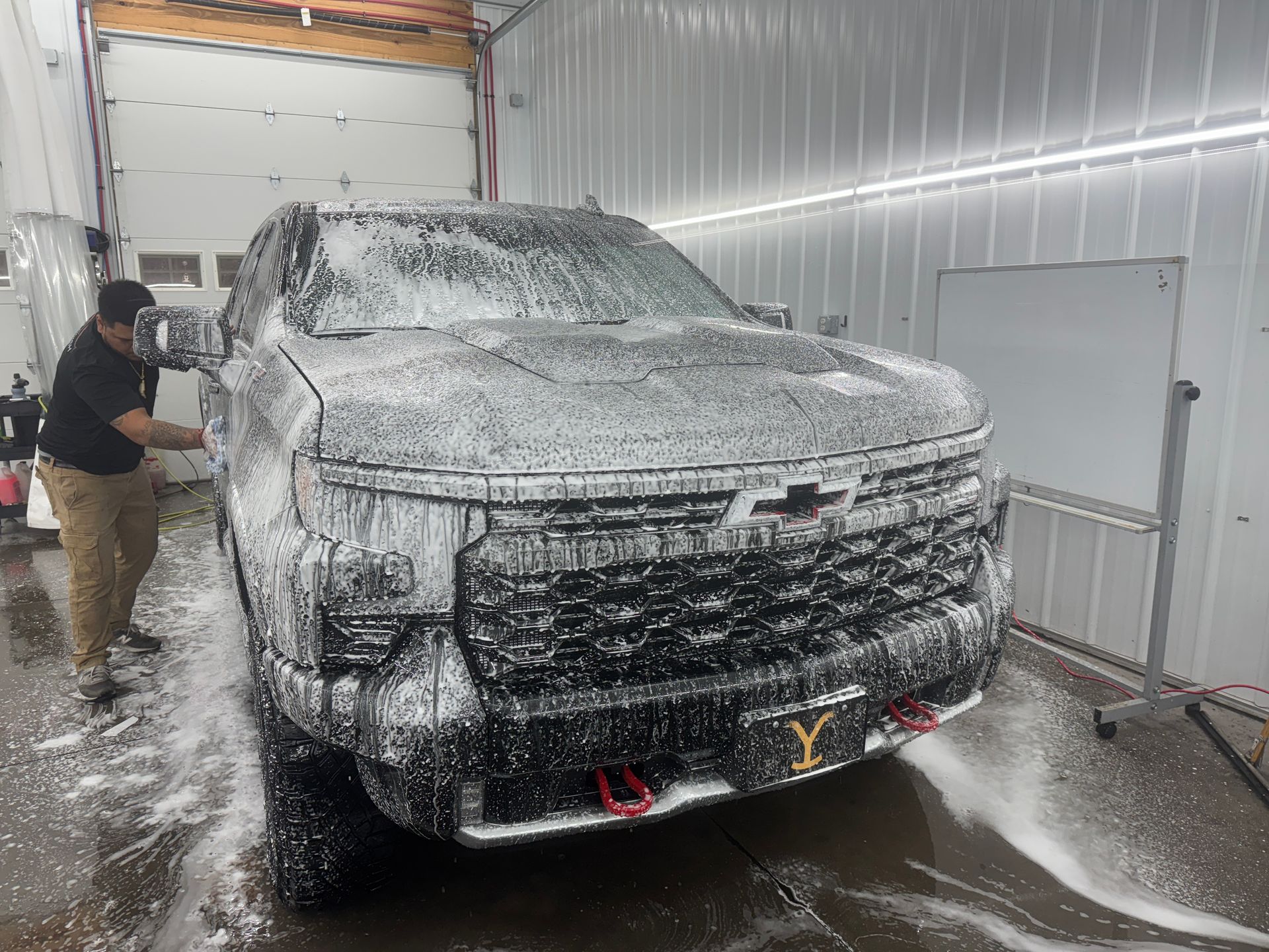 A man is washing a truck with foam in a garage.