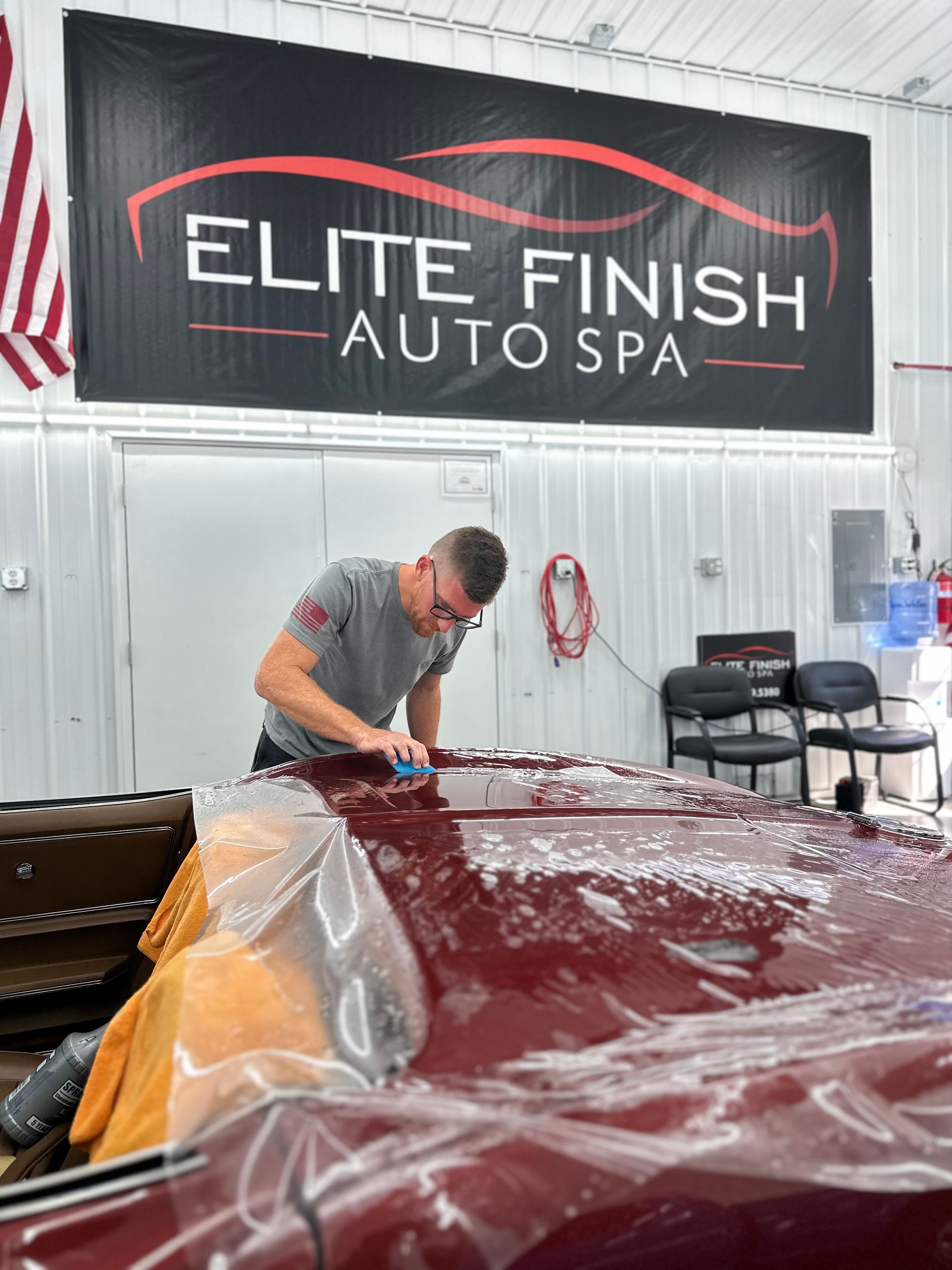 A man is working on a red car in front of a sign that says elite finish auto spa