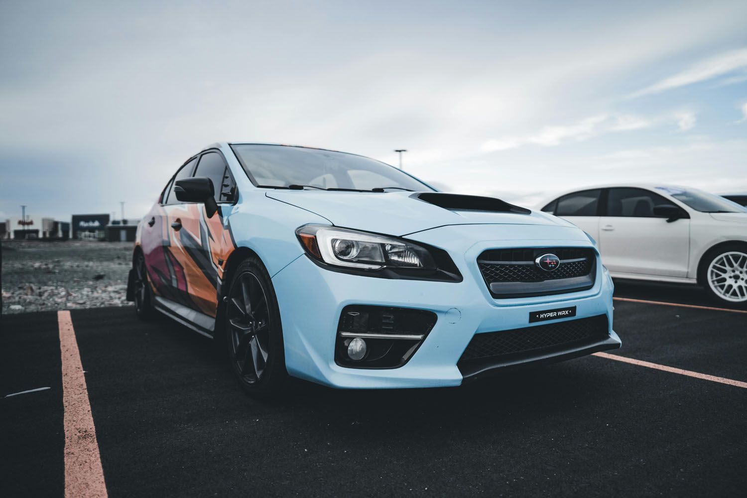 A blue subaru wrx sti is parked in a parking lot next to a white car.