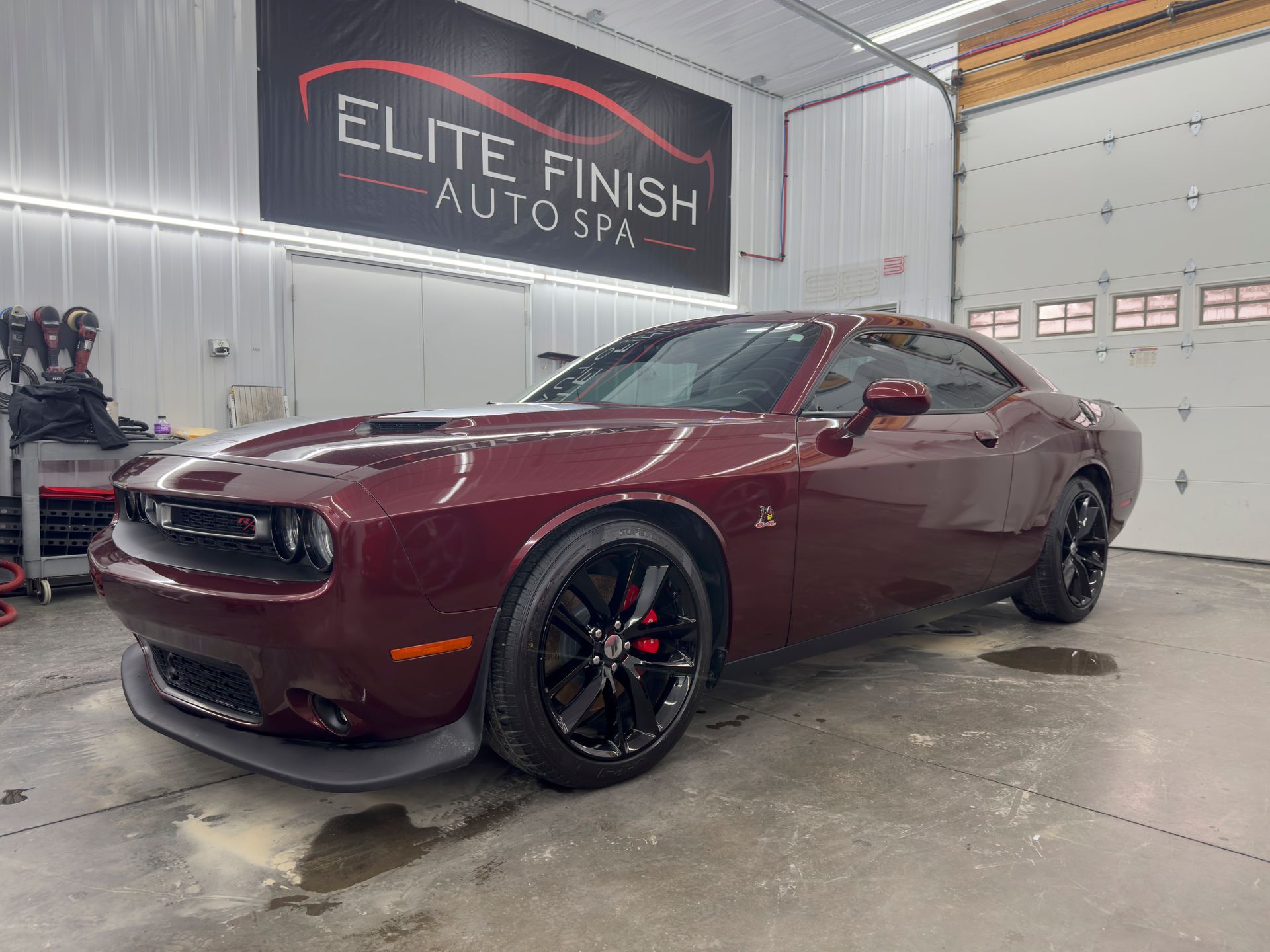 A red dodge challenger is parked in a garage next to a garage door.