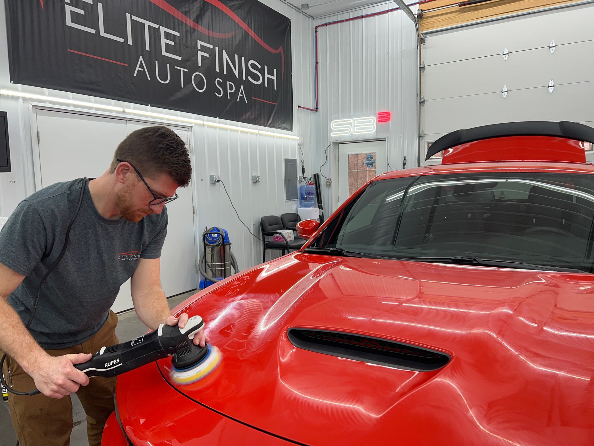 A man is polishing a red car in a garage.