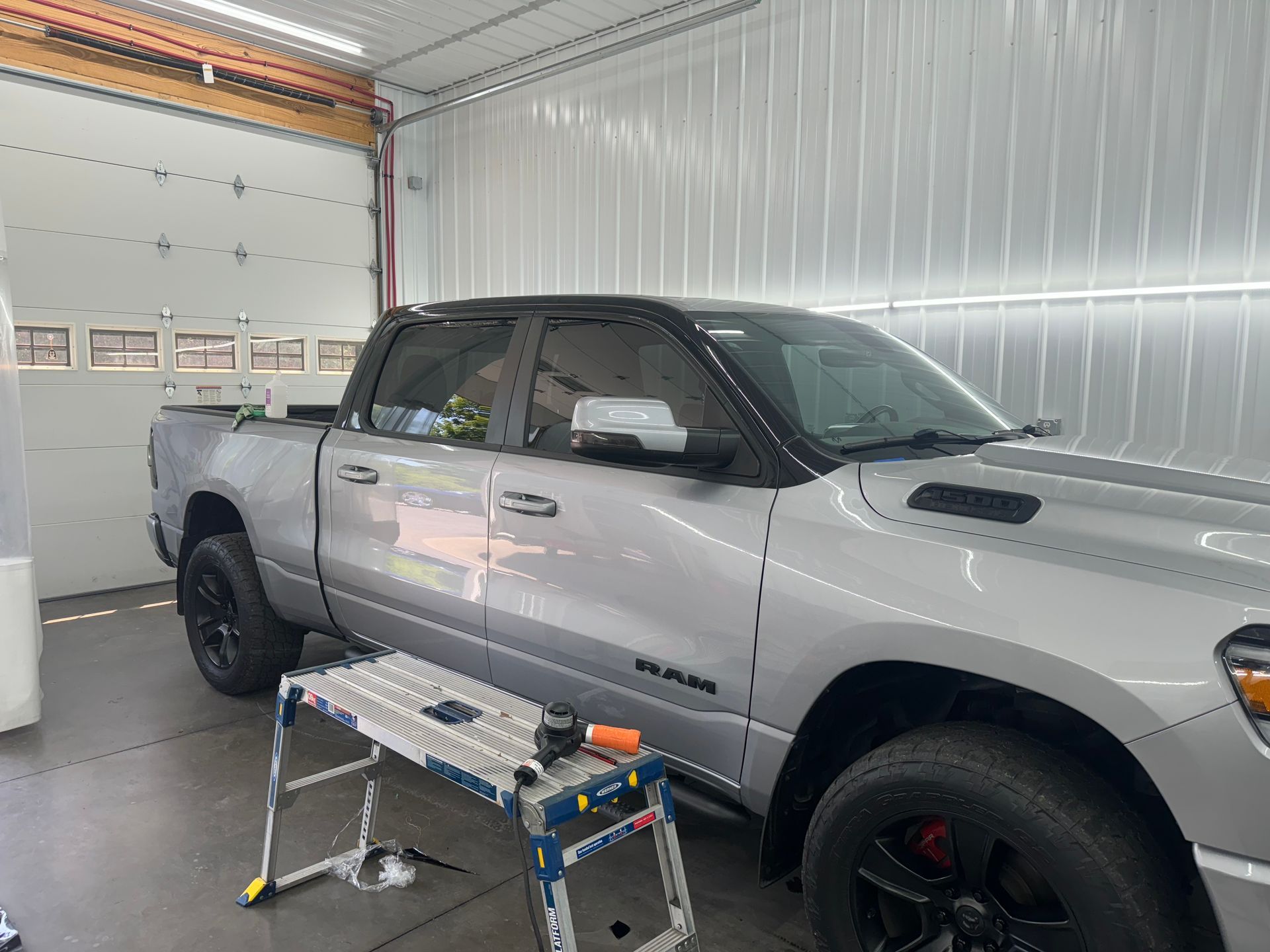 A silver ram truck is parked in a garage next to a ladder.