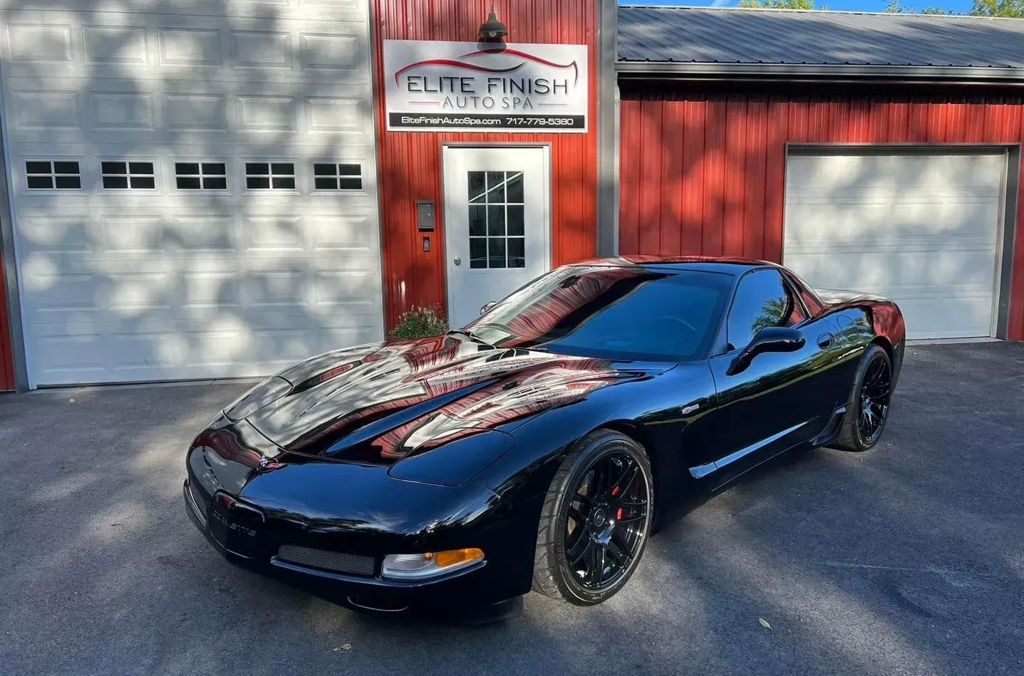 A black corvette is parked in front of a garage.
