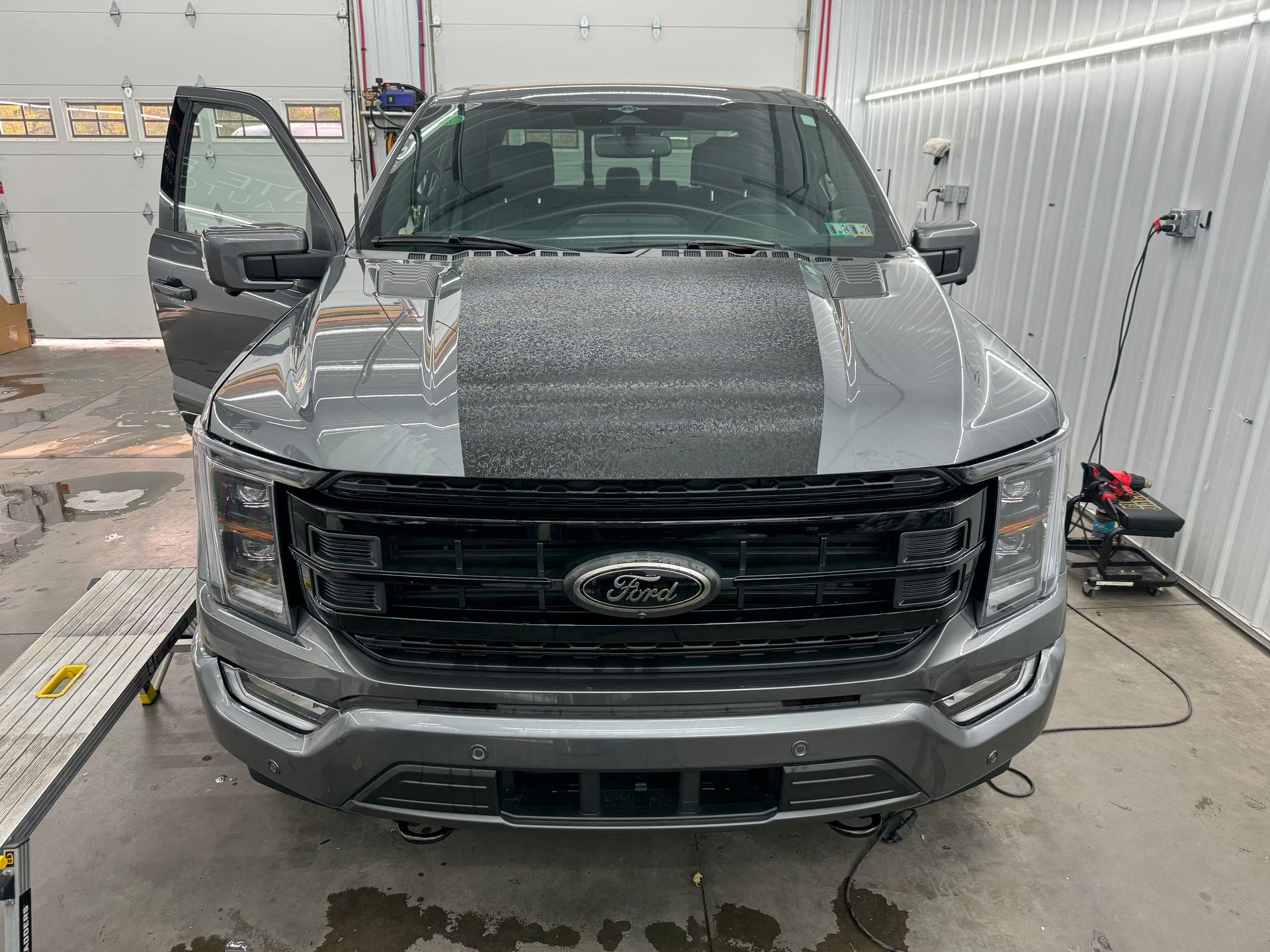 A gray ford f150 is sitting in a garage with its doors open.